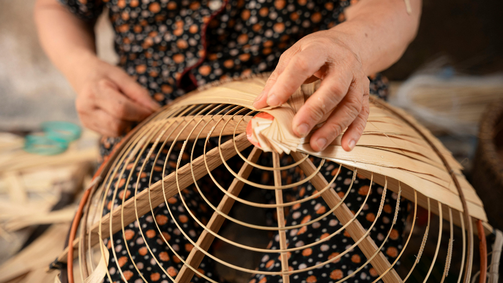 Person working on a woven basket with bamboo and rattan materials, hand craft artisan