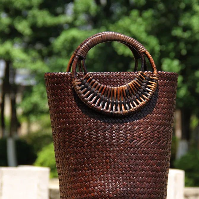 Woven brown bag with decorative handle against a blurred green outdoor background