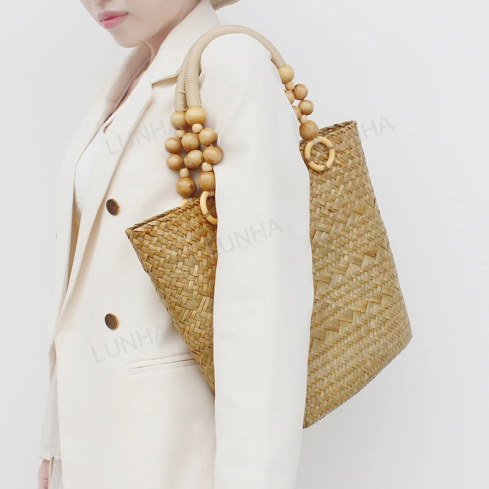 Person wearing a white outfit with a straw handbag featuring wooden beads on a plain background