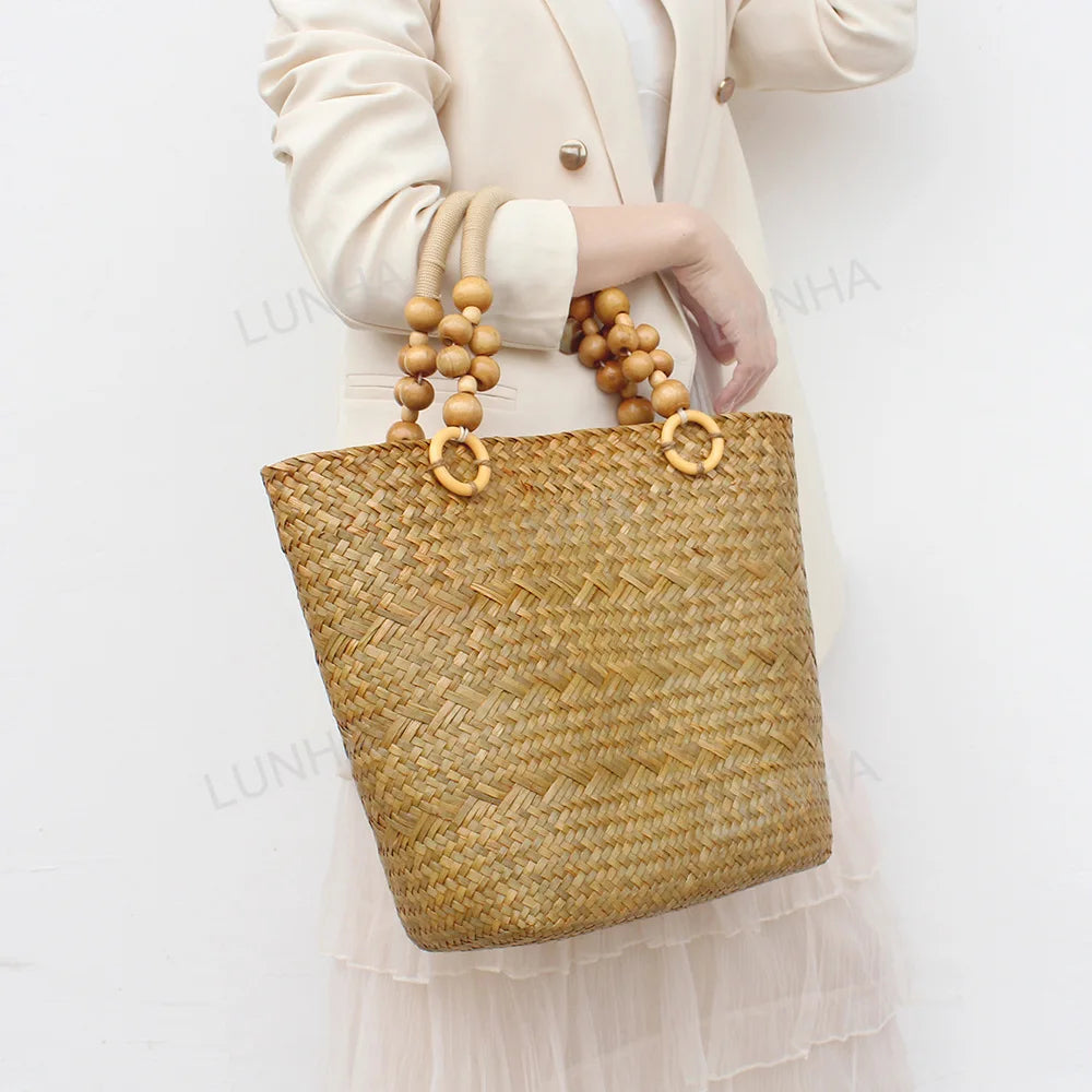 Woven handbag with wooden beads held by a person wearing a white outfit on a light background