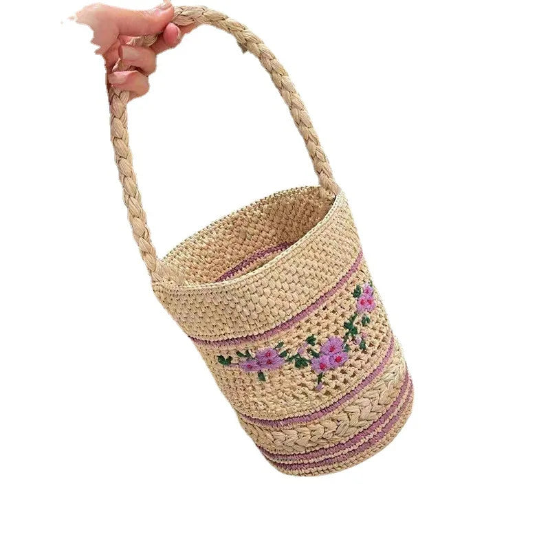 Hand-woven basket with floral embroidery held by a hand on a white background