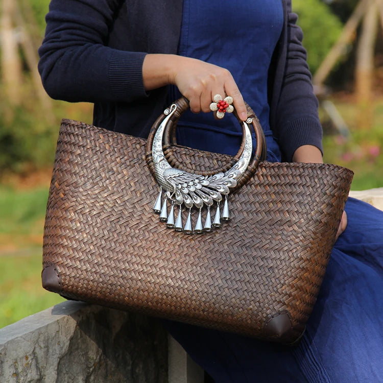 Person holding a woven handbag with decorative handle in an outdoor setting