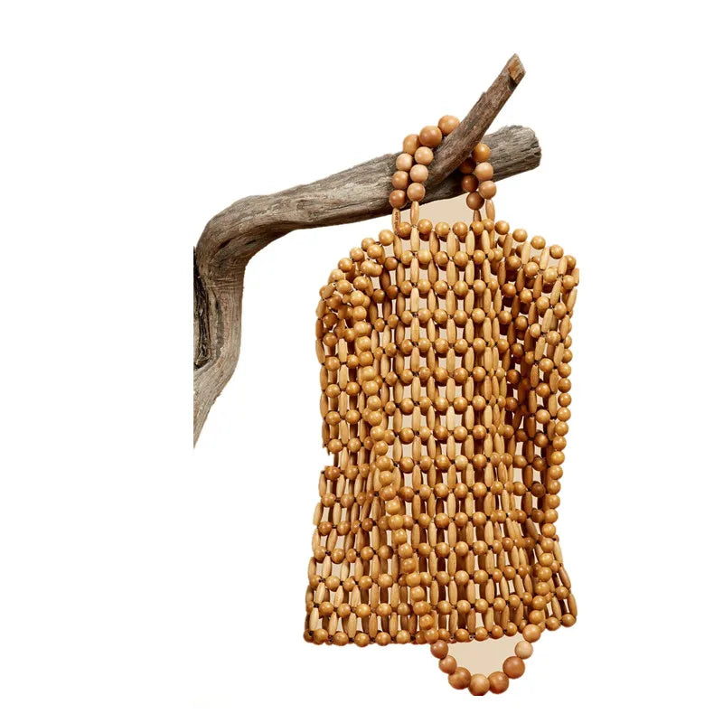 A natural wood bead fringe bag hanging from a rustic branch against a plain white background.