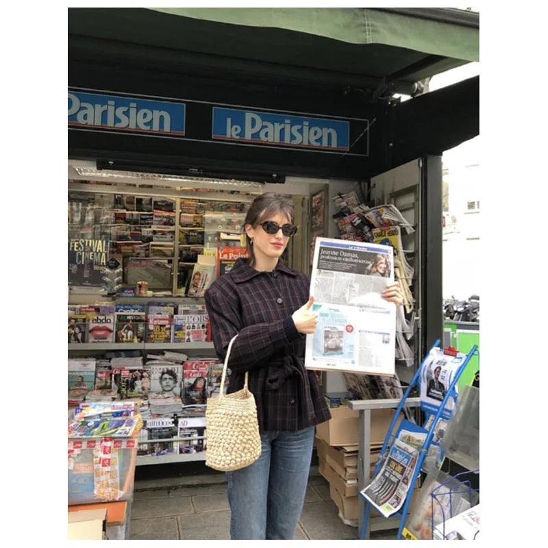Woman reading a newspaper in front of a Parisian newspaper stand.