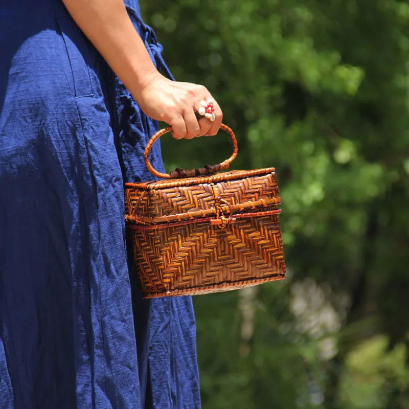 Person holding a woven brown handbag with a blurred green background