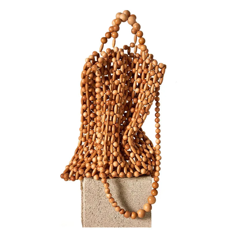 A natural wood beaded handbag with a structured top handle and cascading bead strands, displayed on a textured beige block against a white background.