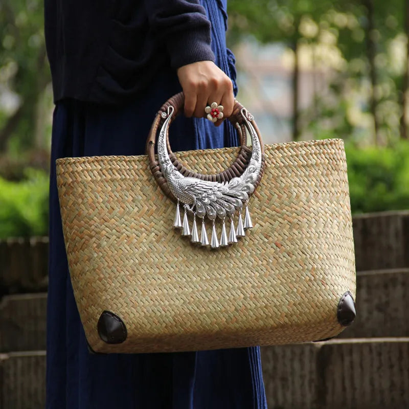 Person holding a woven handbag with decorative handle outdoors