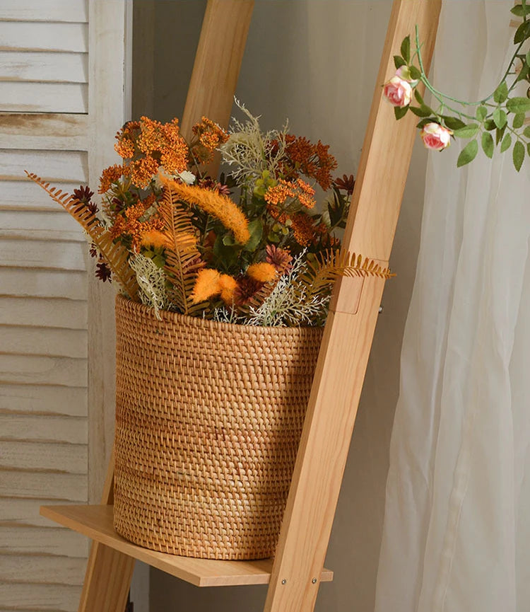 Wicker basket with autumnal flowers on a wooden ladder against a neutral wall.
