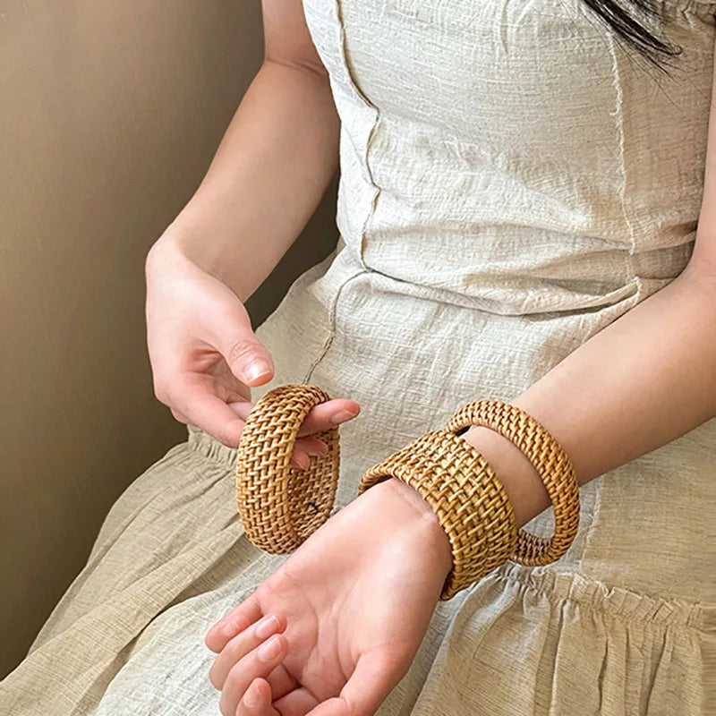 Person wearing gold woven arm bands against a neutral background