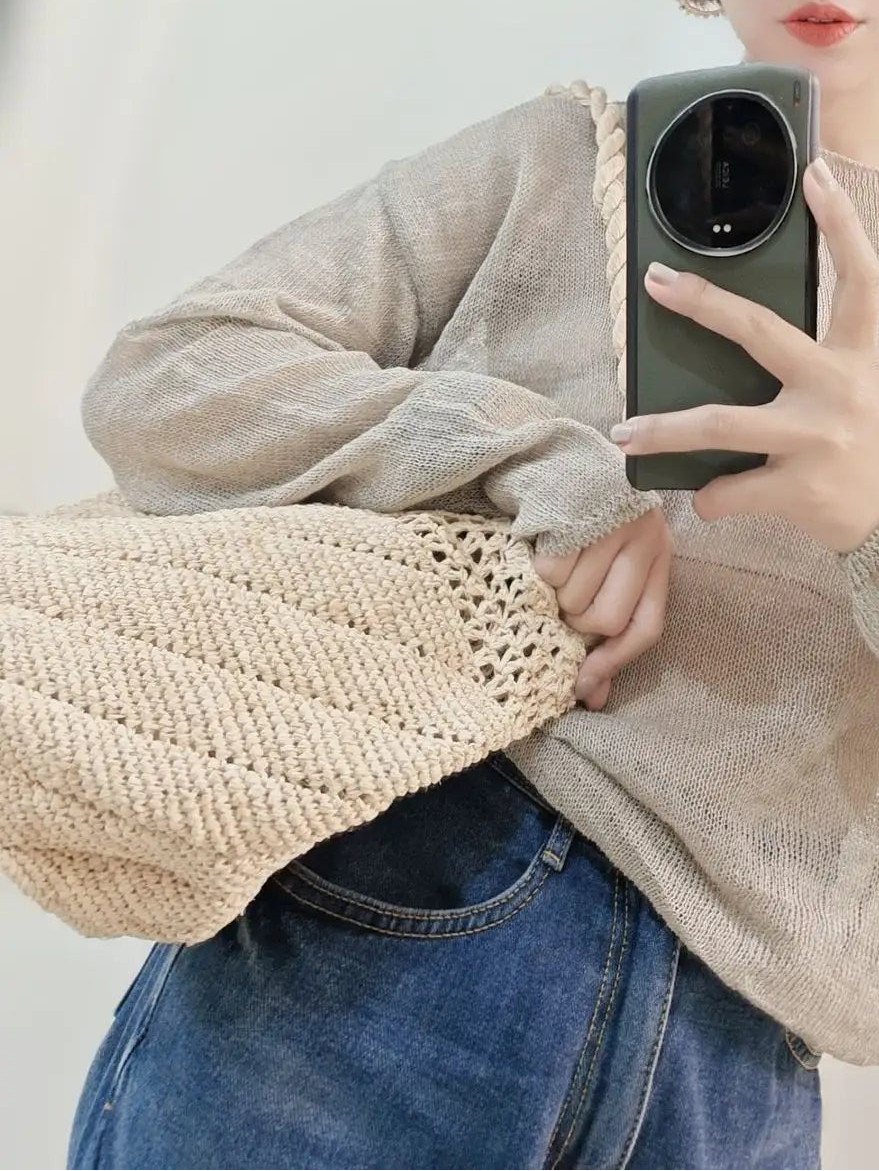 Person wearing a beige sweater and straw hat, holding a phone in a neutral setting