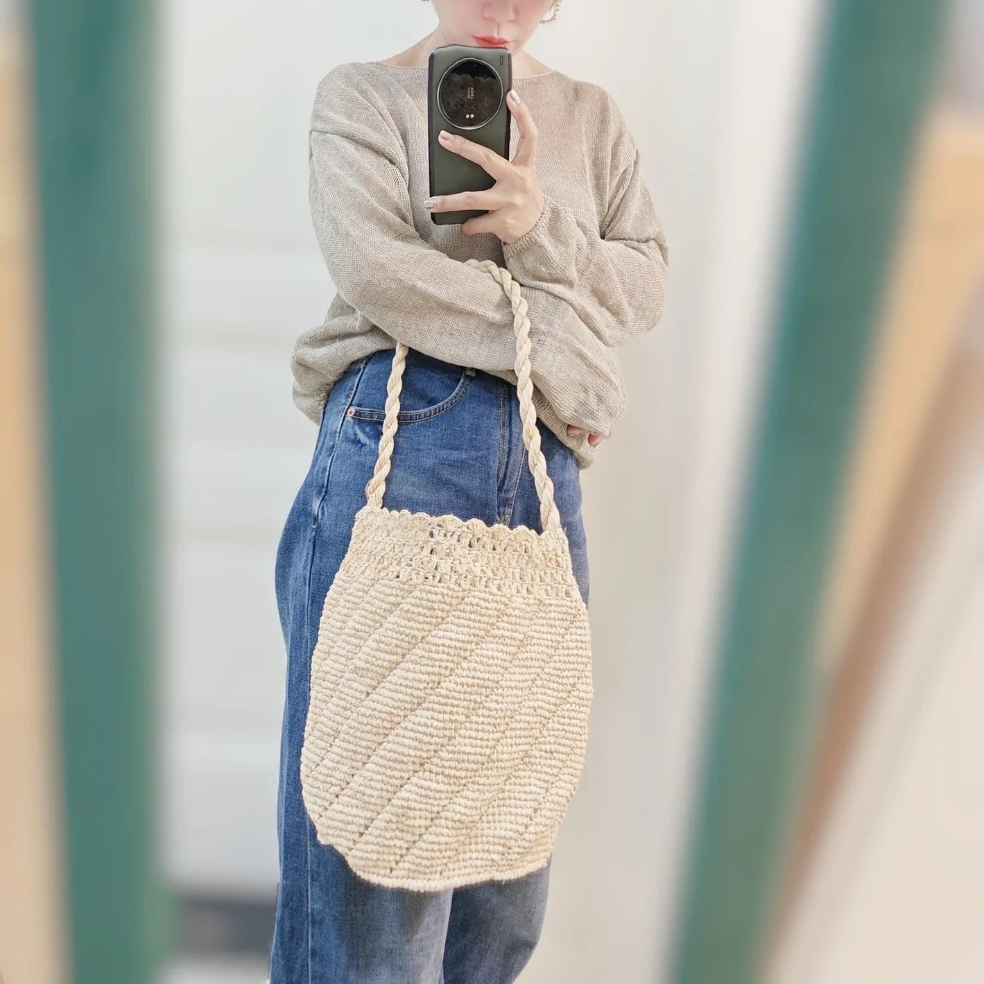 Person taking a mirror selfie wearing a straw hat, beige sweater, blue jeans, and a woven handbag.