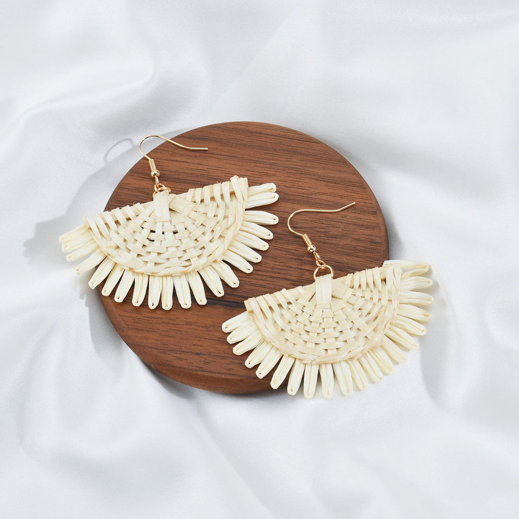 Cream-colored fan-shaped earrings on a wooden board with a white fabric background