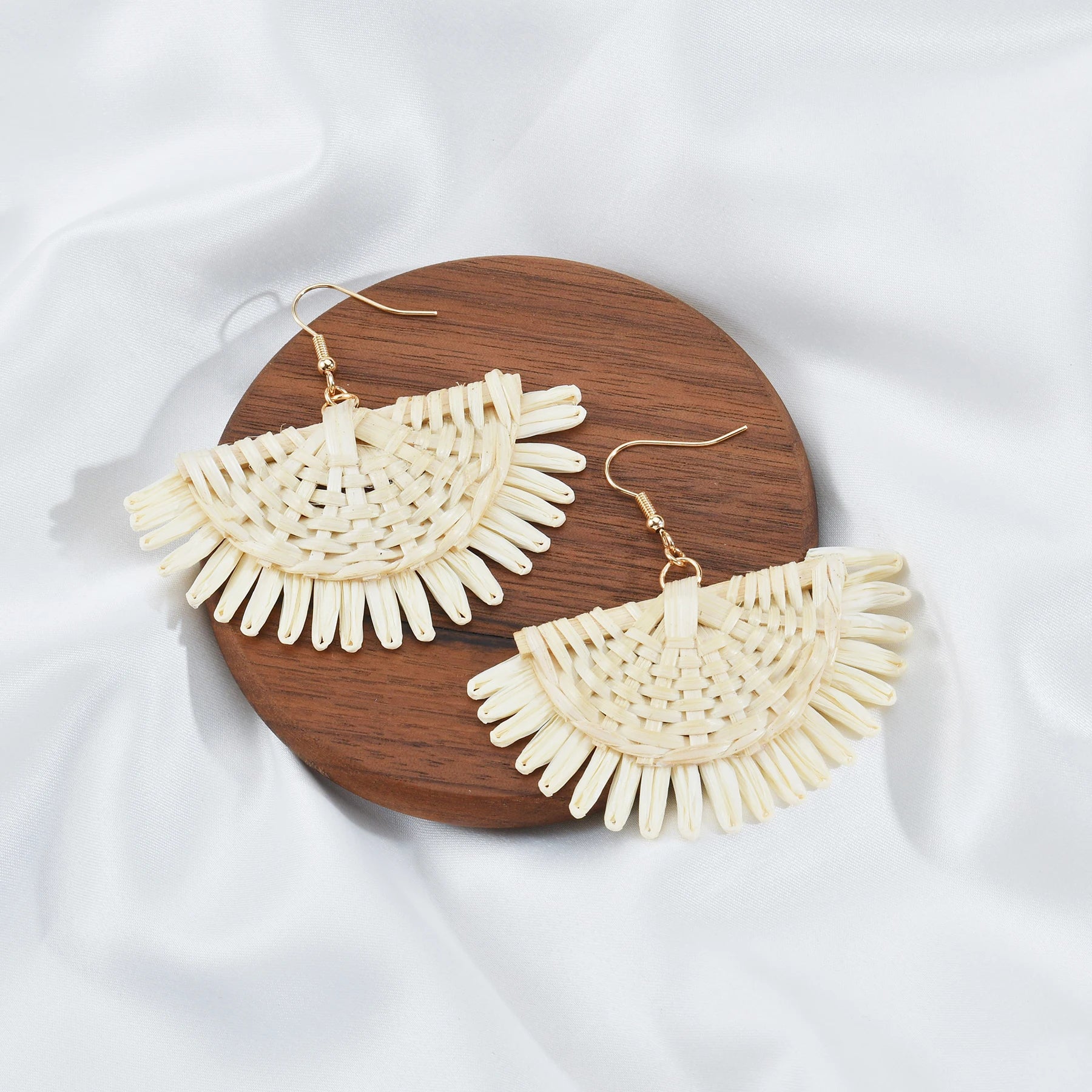 Cream-colored fan-shaped earrings on a wooden board with a white fabric background