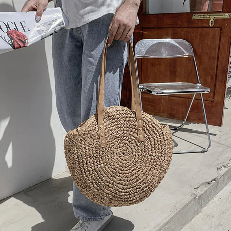 Person holding a woven bag outdoors with a chair and wall in the background