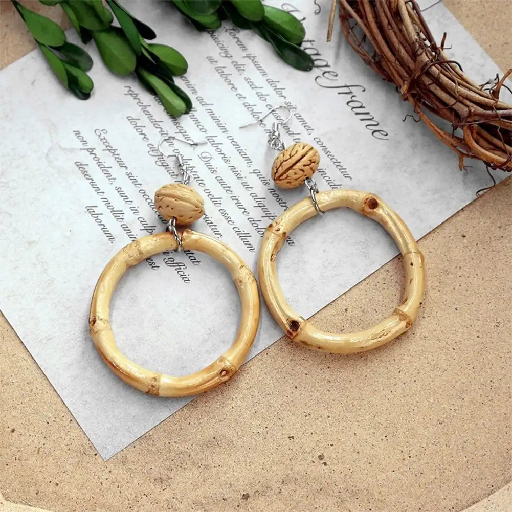 Bamboo hoop earrings with wooden accents on a textured surface with greenery.