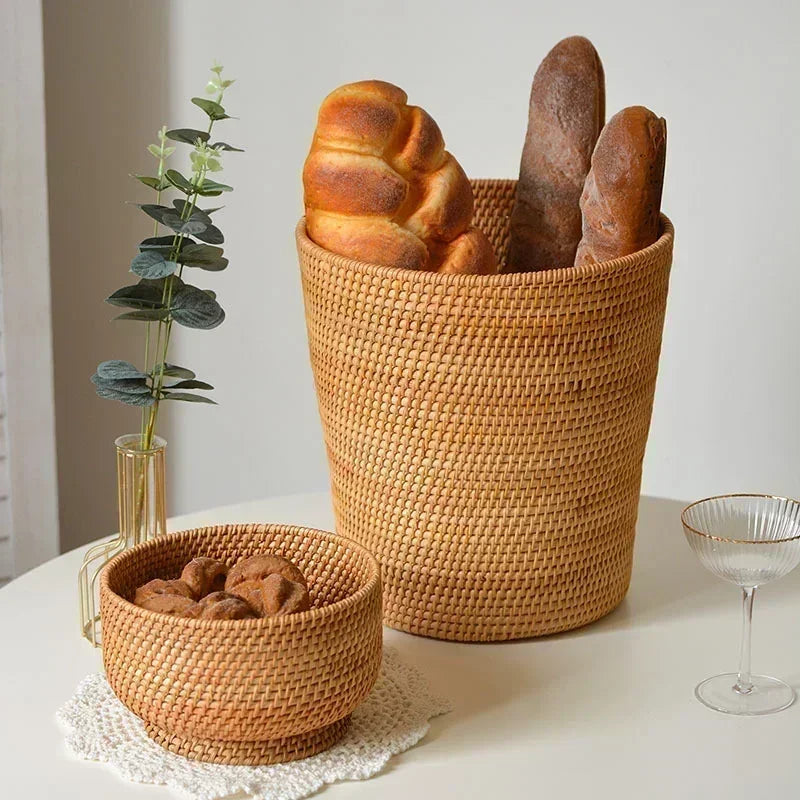 Two RATTAN woven baskets with bread and cookies on a table with a plant and glass in the background.