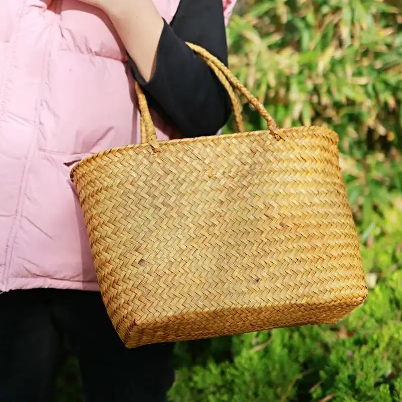 Person holding a woven straw bag outdoors with greenery in the background