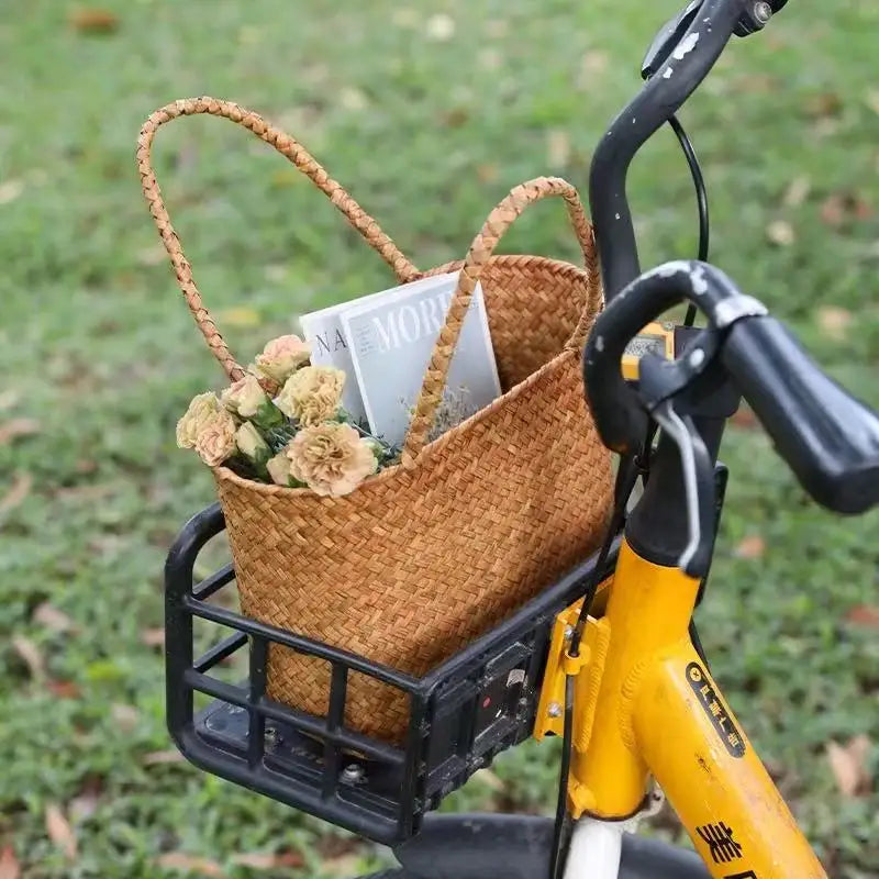 Wicker basket on a yellow bicycle with flowers and a newspaper against a grassy background