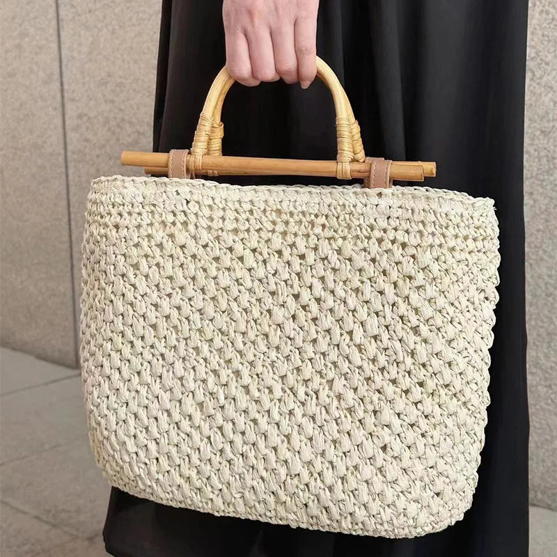 Woven handbag with bamboo handle held by a person against a neutral background