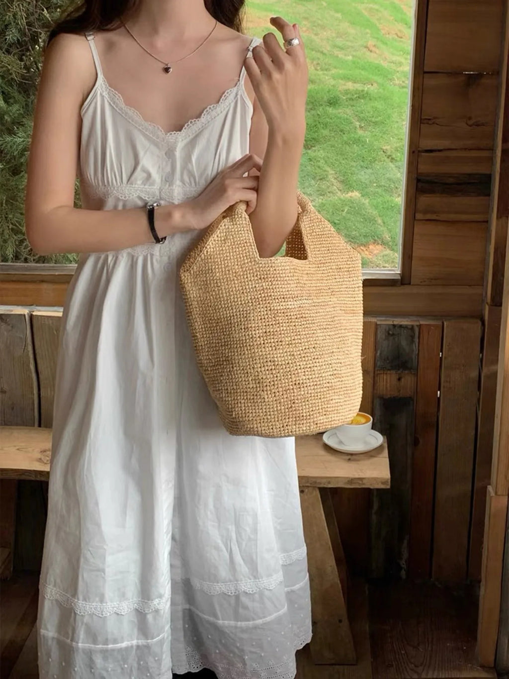 Woman in a white dress holding a straw bag in a rustic setting