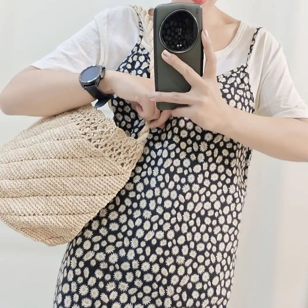 Person wearing a straw hat and holding a phone, standing against a white wall.