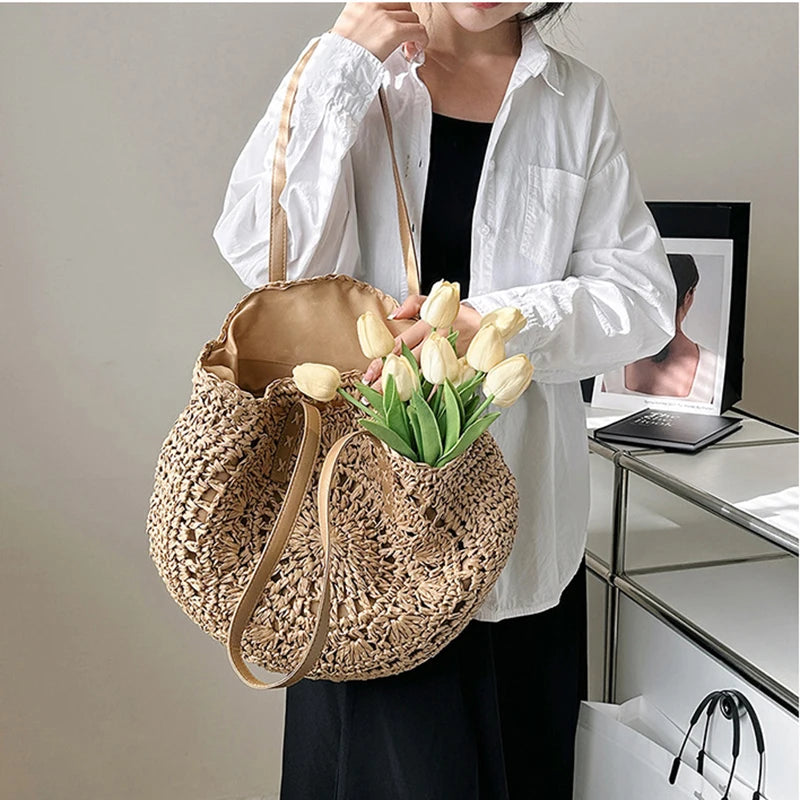 Person holding a woven bag with flowers, wearing a white shirt and black pants, in an indoor setting.
