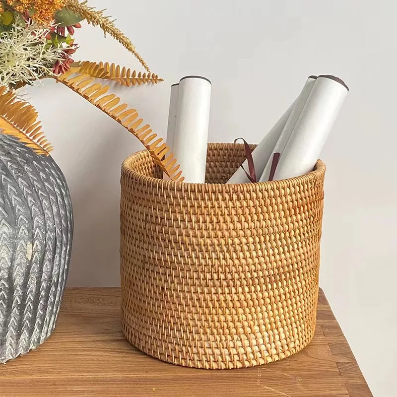 Woven basket with rolled-up papers on a wooden surface next to a plant