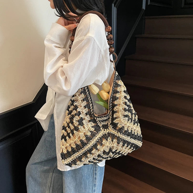 Person holding a black and beige woven handbag with a neutral background