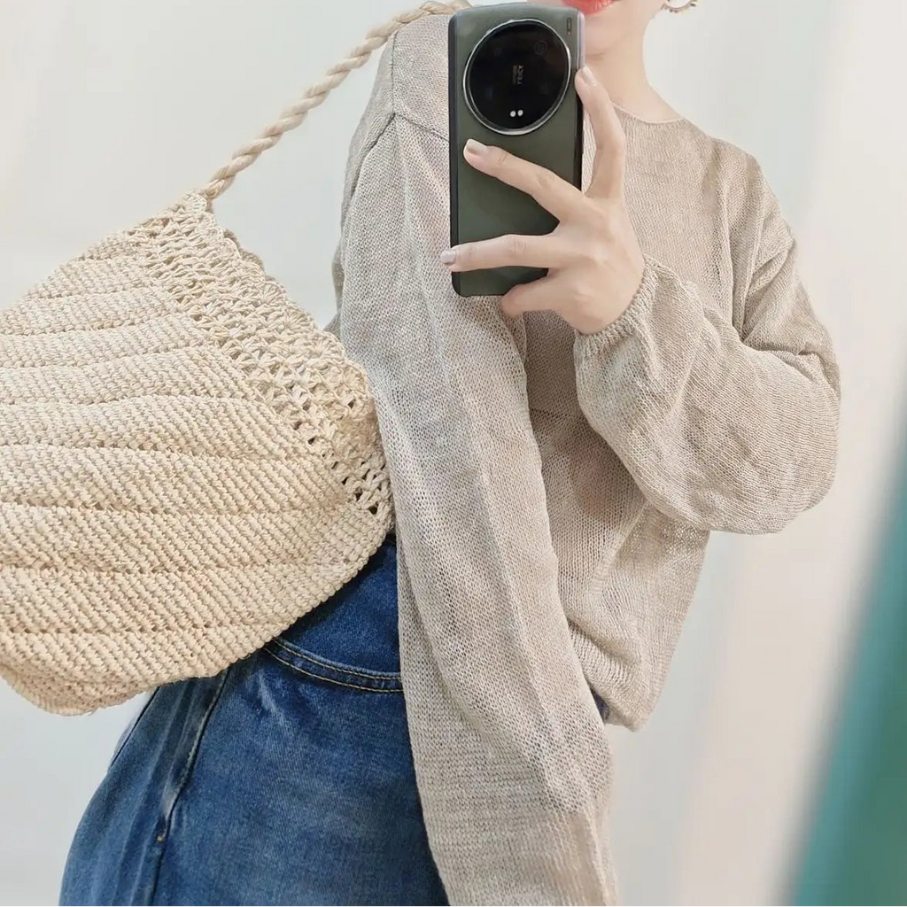 Person wearing a straw hat and holding a woven bag, taking a mirror selfie.