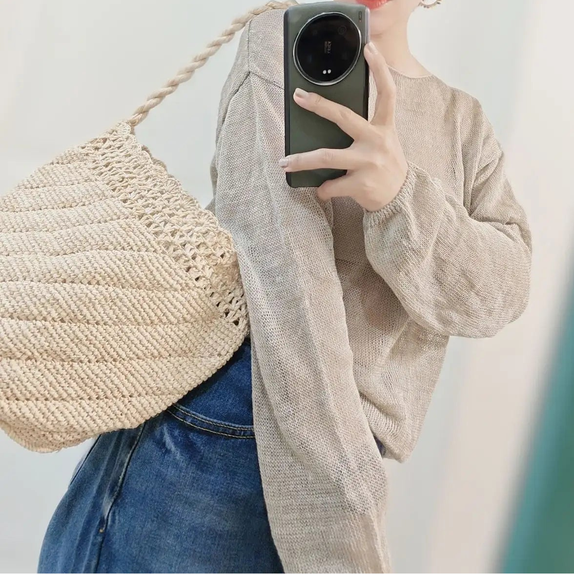 Person wearing a straw hat and holding a woven bag, taking a mirror selfie.