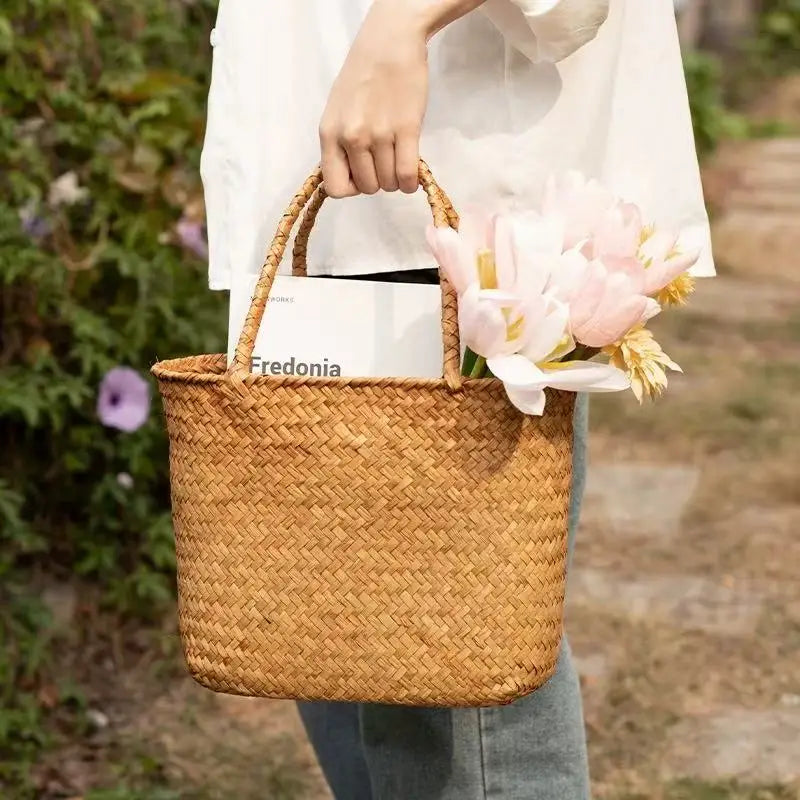 Person holding a woven basket with flowers and a book titled 'Fredonia' outdoors.