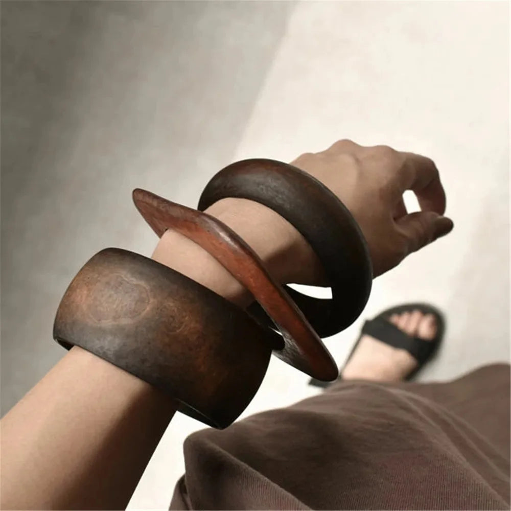 Close-up of a person wearing two wooden bangles on a neutral background