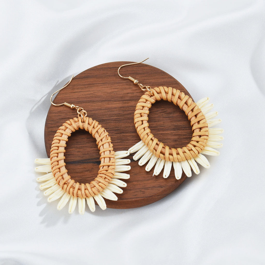 Pair of raffia hoop earrings with white accents on a wooden board.