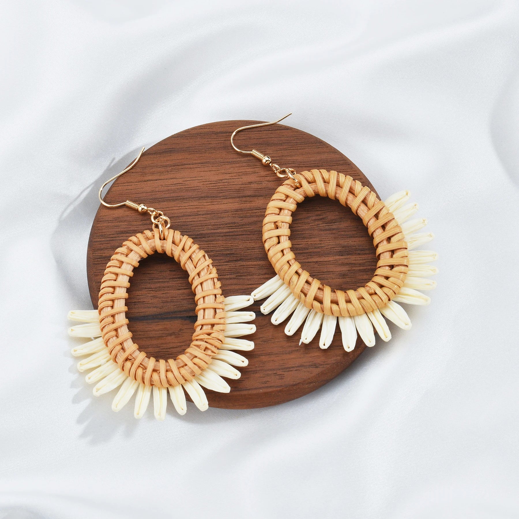 Pair of raffia hoop earrings with white accents on a wooden board.