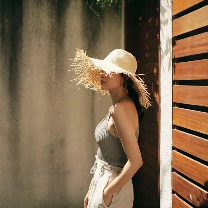 Woman wearing a wide-brimmed straw hat in a sunlit outdoor setting.