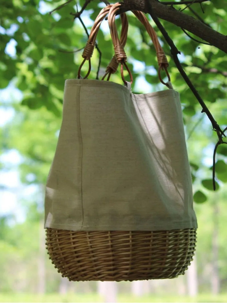 Beige fabric bag with wicker base hanging from a tree branch