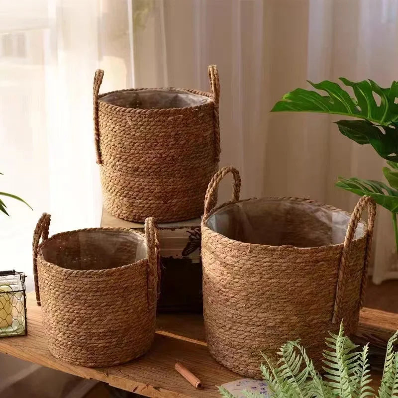 Three woven baskets on a wooden surface with plants in the background