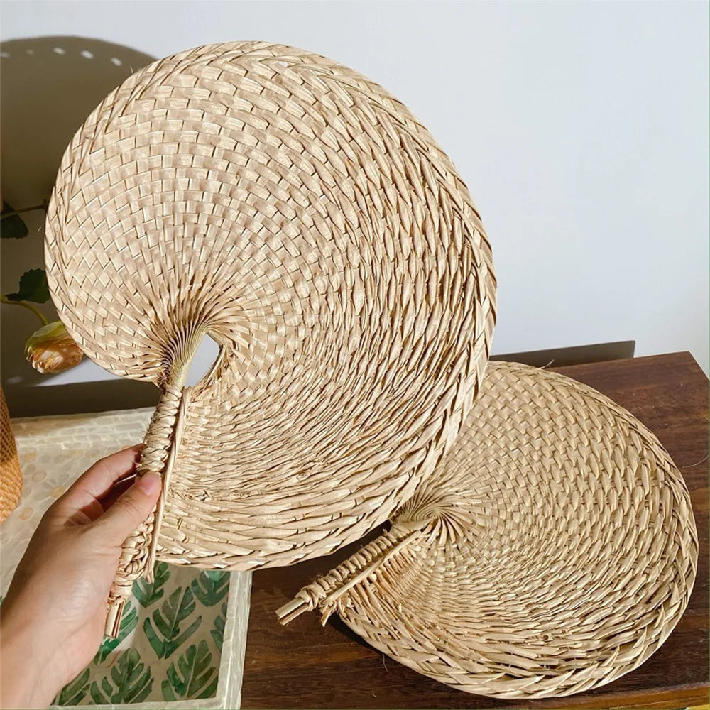 Woven straw hat held by a hand on a wooden surface with a neutral background