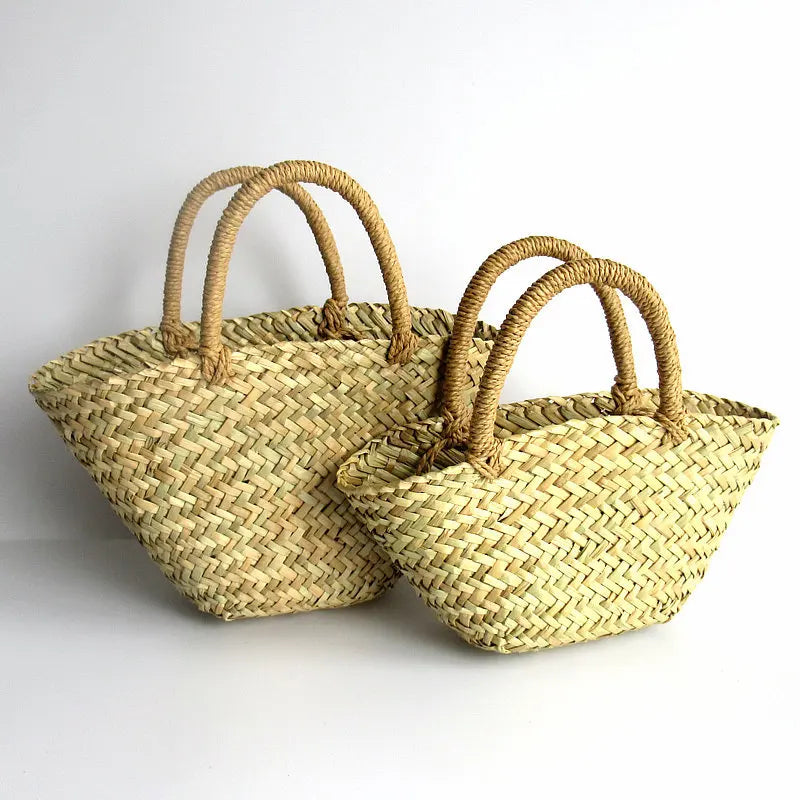 Two natural straw woven tote bags with curved handles, displayed on a clean white background.