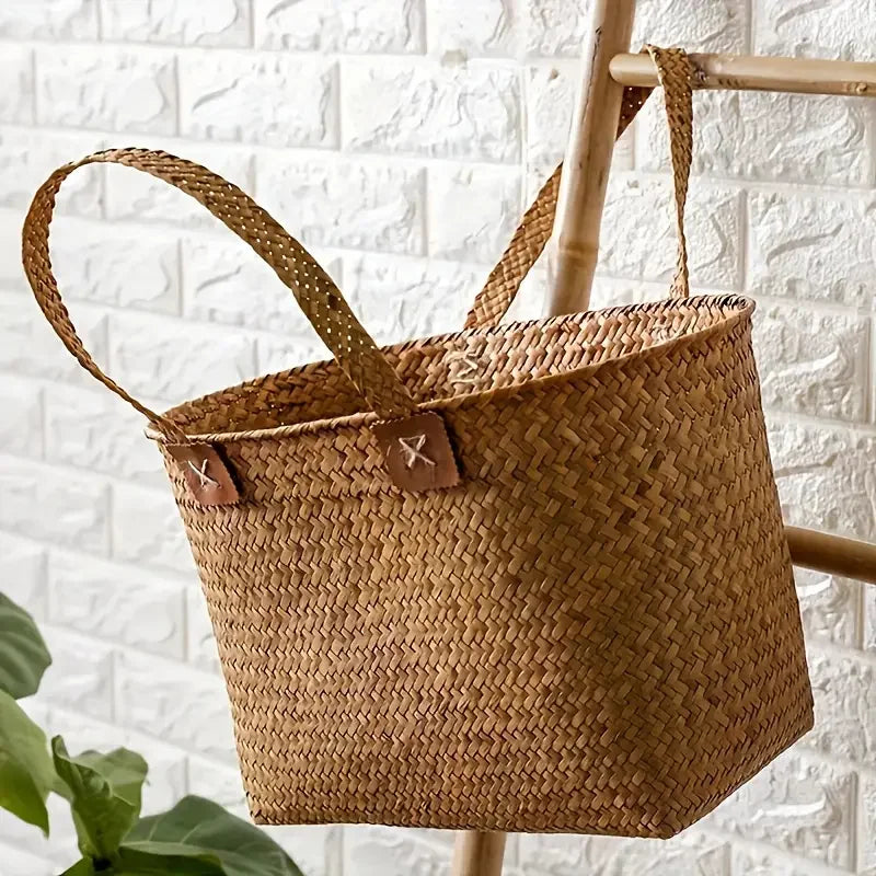Woven brown basket with leather straps against a white brick wall.