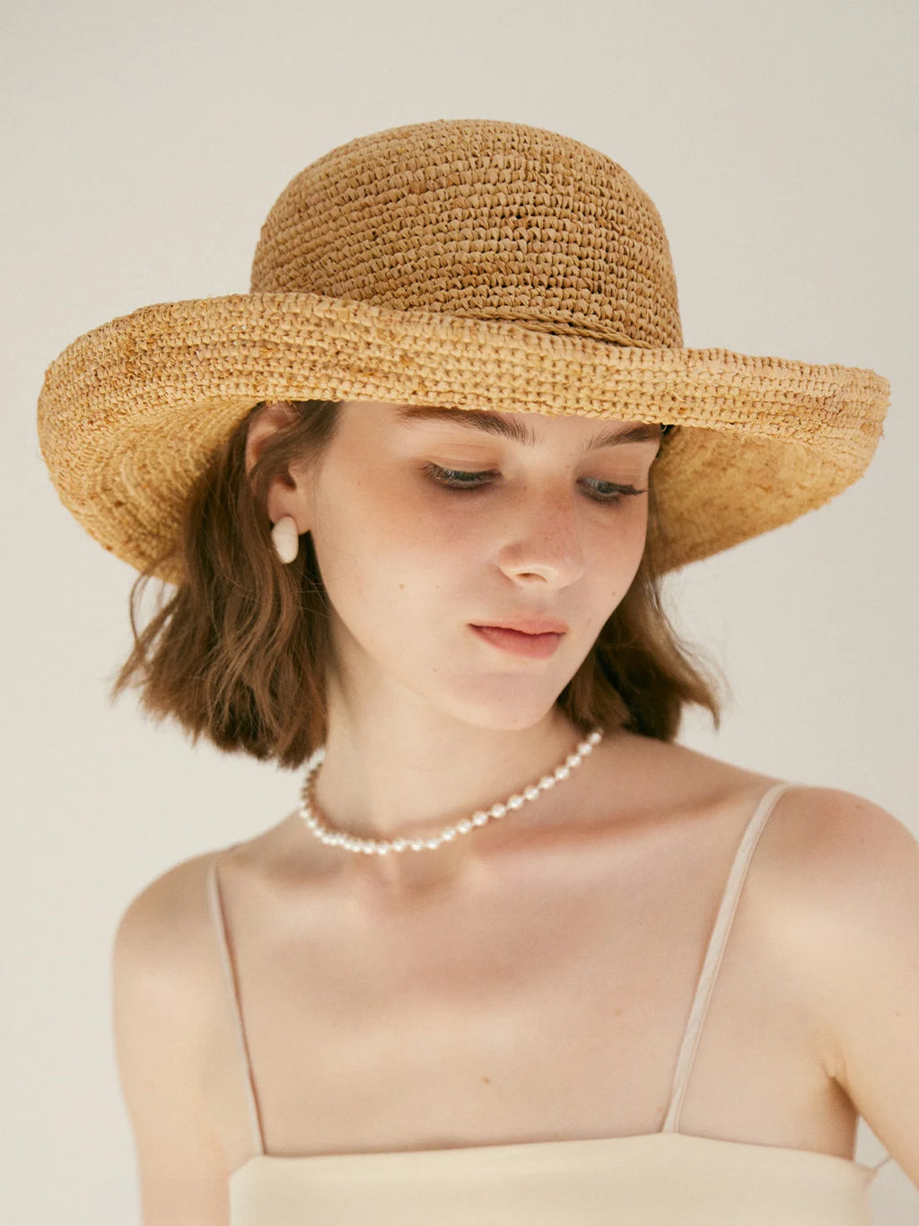 Woman wearing a straw hat and pearl necklace against a plain background