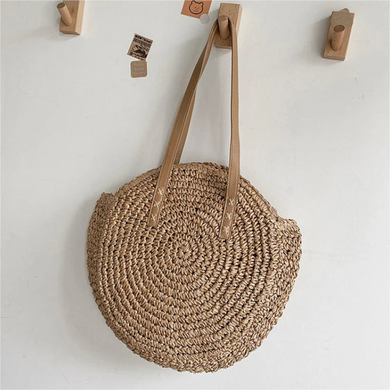 Round woven bag with leather straps hanging on a wall with hooks.
