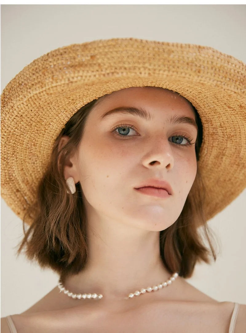 Woman wearing a straw hat and pearl necklace against a plain background