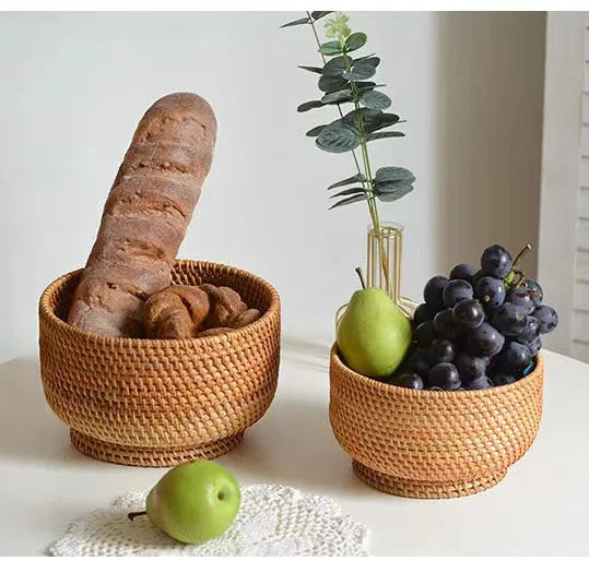 Two woven baskets with bread, grapes, and pears on a white surface.