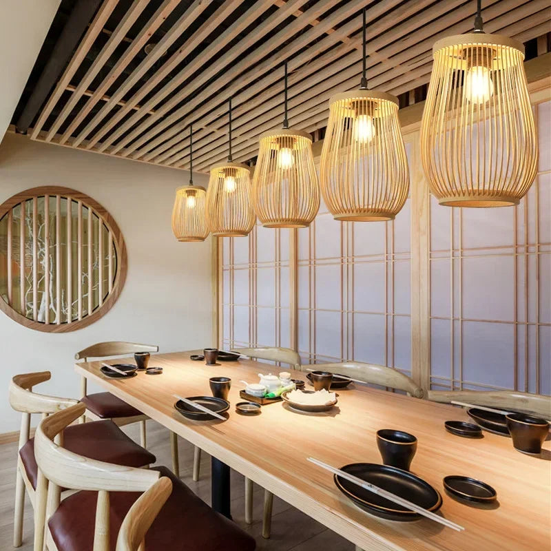 Dining area with a long wooden table set for a meal, featuring bowls and chopsticks, with pendant lights hanging above.