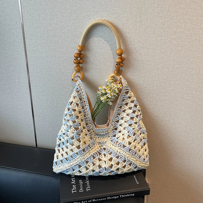 Crocheted handbag with wooden handle and flowers on a book against a neutral background