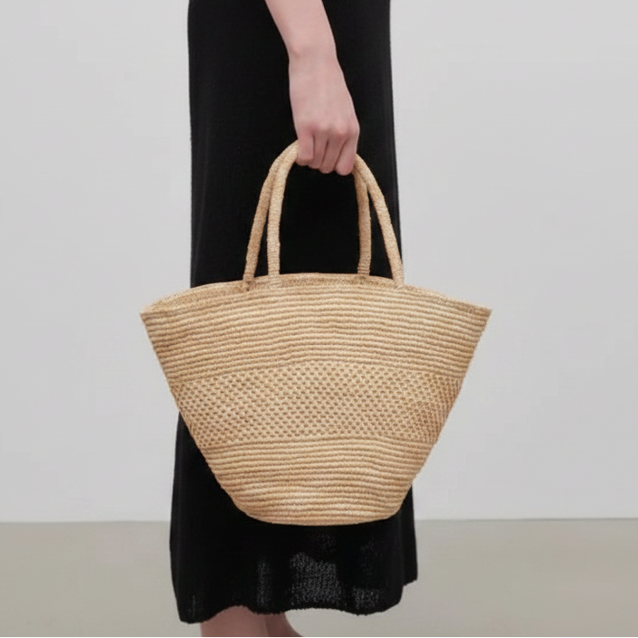 Person holding a woven straw bag against a plain background