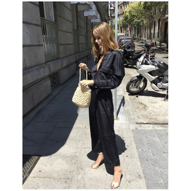 Woman in black outfit holding a woven handbag on a city street.