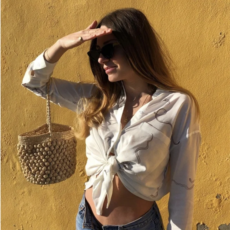 Woman in a white shirt and sunglasses standing against a yellow wall with a woven basket.
